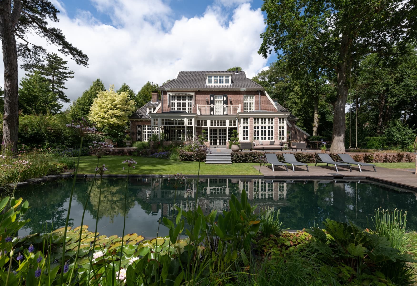 Tuinzijde villa met bakstenen gevel, ramen en natuurvijver met waterplanten