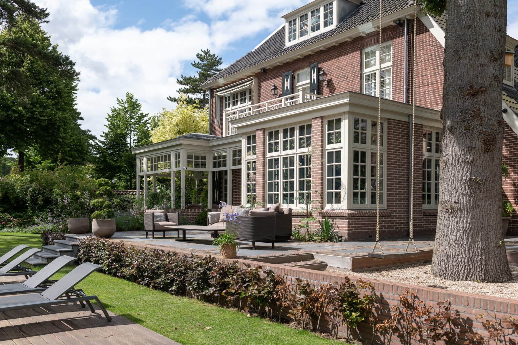 Bakstenen woning met glazen serre, loungegebied en haagafscheiding