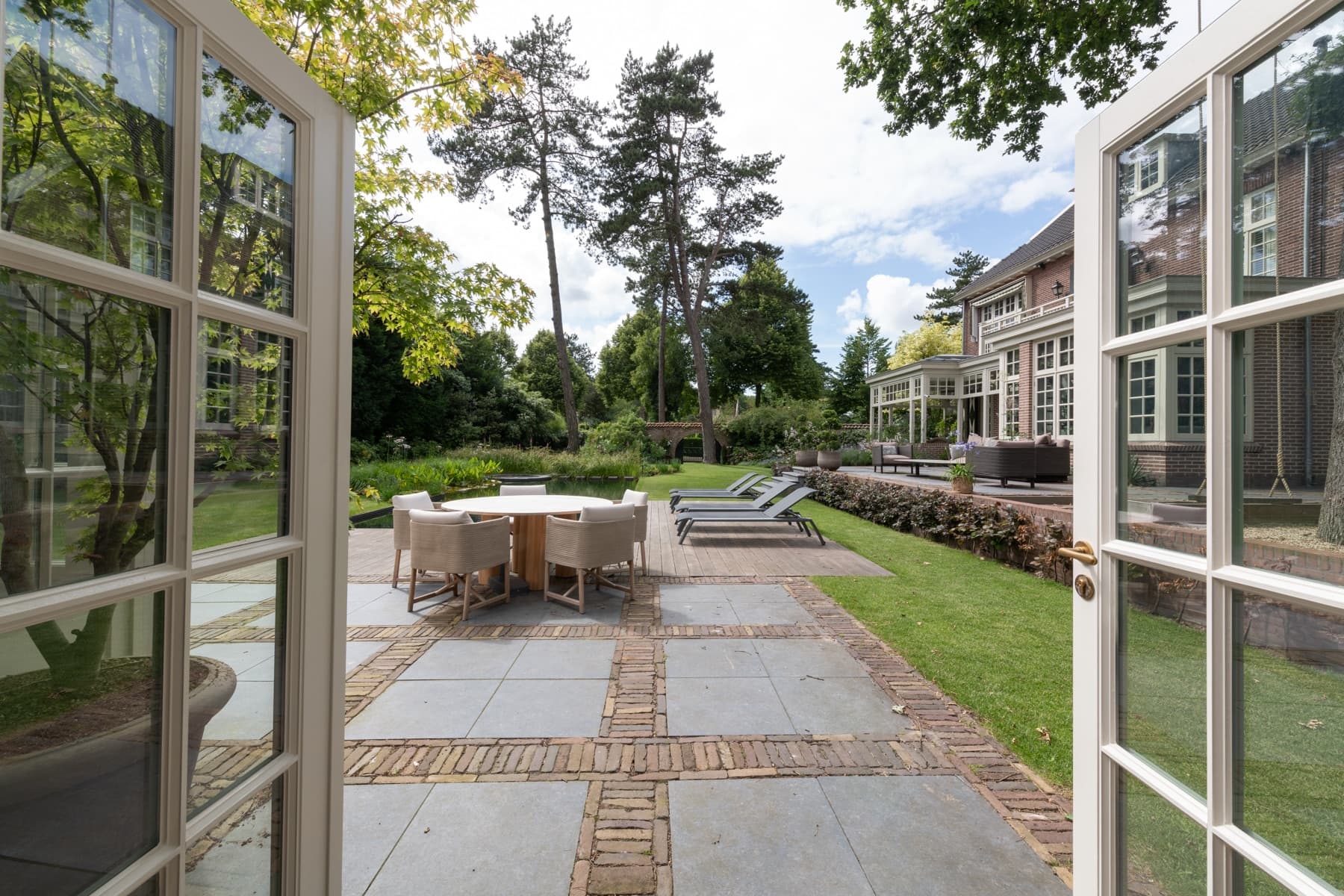 Terras met natuurstenen tegels, loungestoelen en uitzicht op tuin