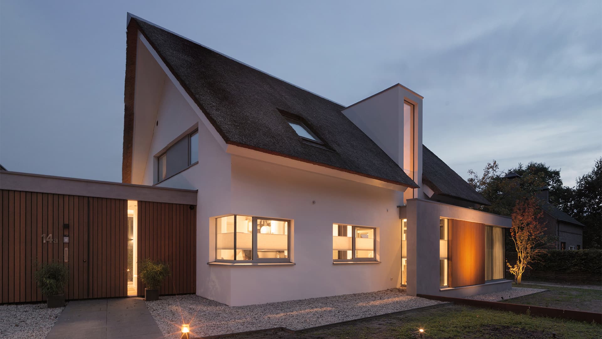 Moderne villa met rietgedakt dak, houten horizontale gevelbekleding, avondverlichting