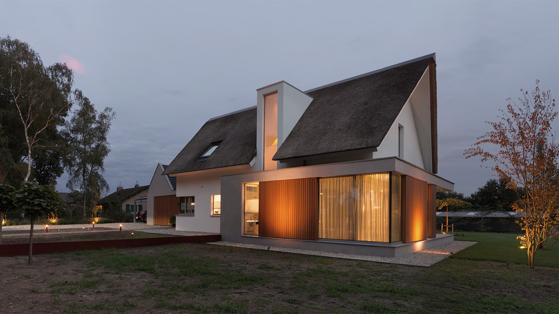 Moderne villa met rietgedekte daken, witte en grijs gevelbekleding, avondverlichting