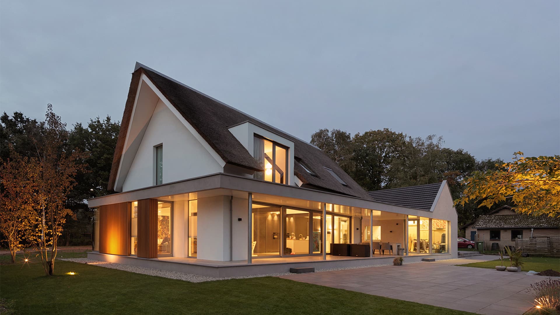 Moderne villa met rietgedakt dak, houten accenten, avondverlichting, terras