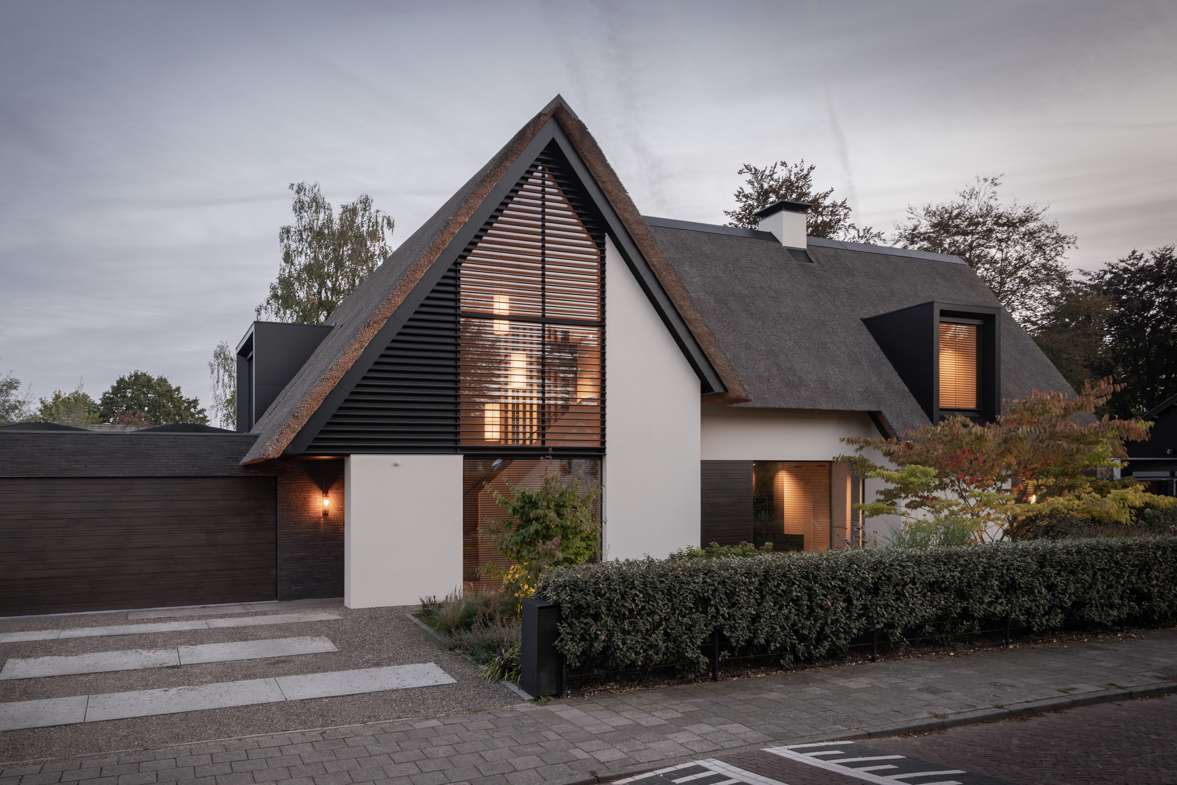 Zwart-witte rietgedekte villa met houten jaloeziën en landscaping