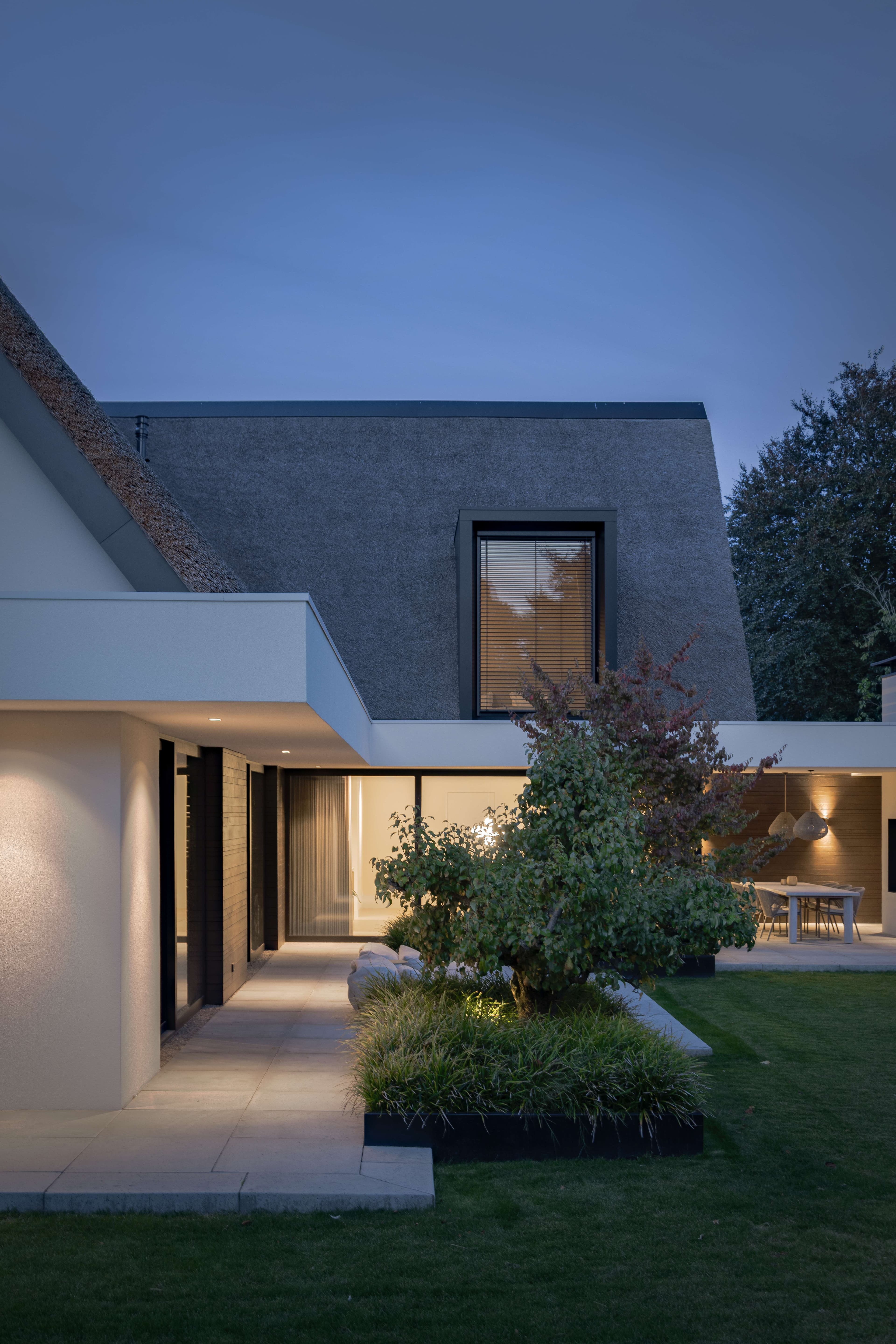 Rietgedekte woning met grote glazen gevel, wit en zwart contrast, oprit in grijs