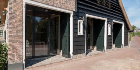 Gevel bakstenen gebouw met groene schuifdeuren en witte raamkozijnen