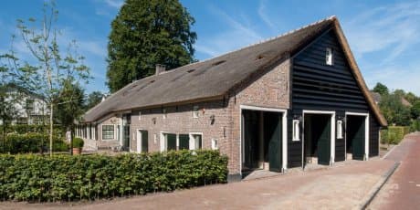 Buitenkant bakstenen schuur met rietdak en grote glazen schuifdeuren