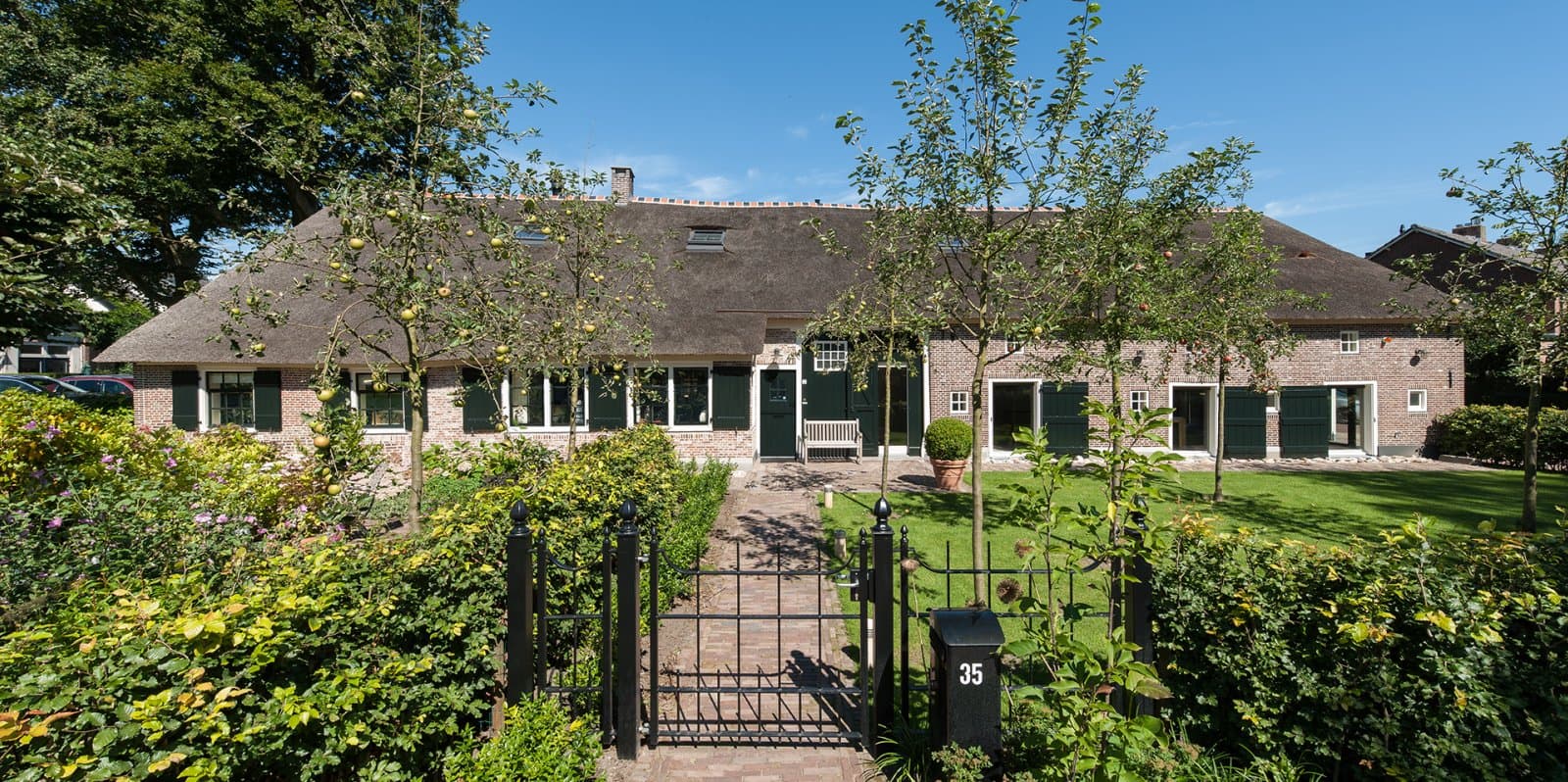 Voorgevel rietgedekt huis met toegangspoort en tuinplanten