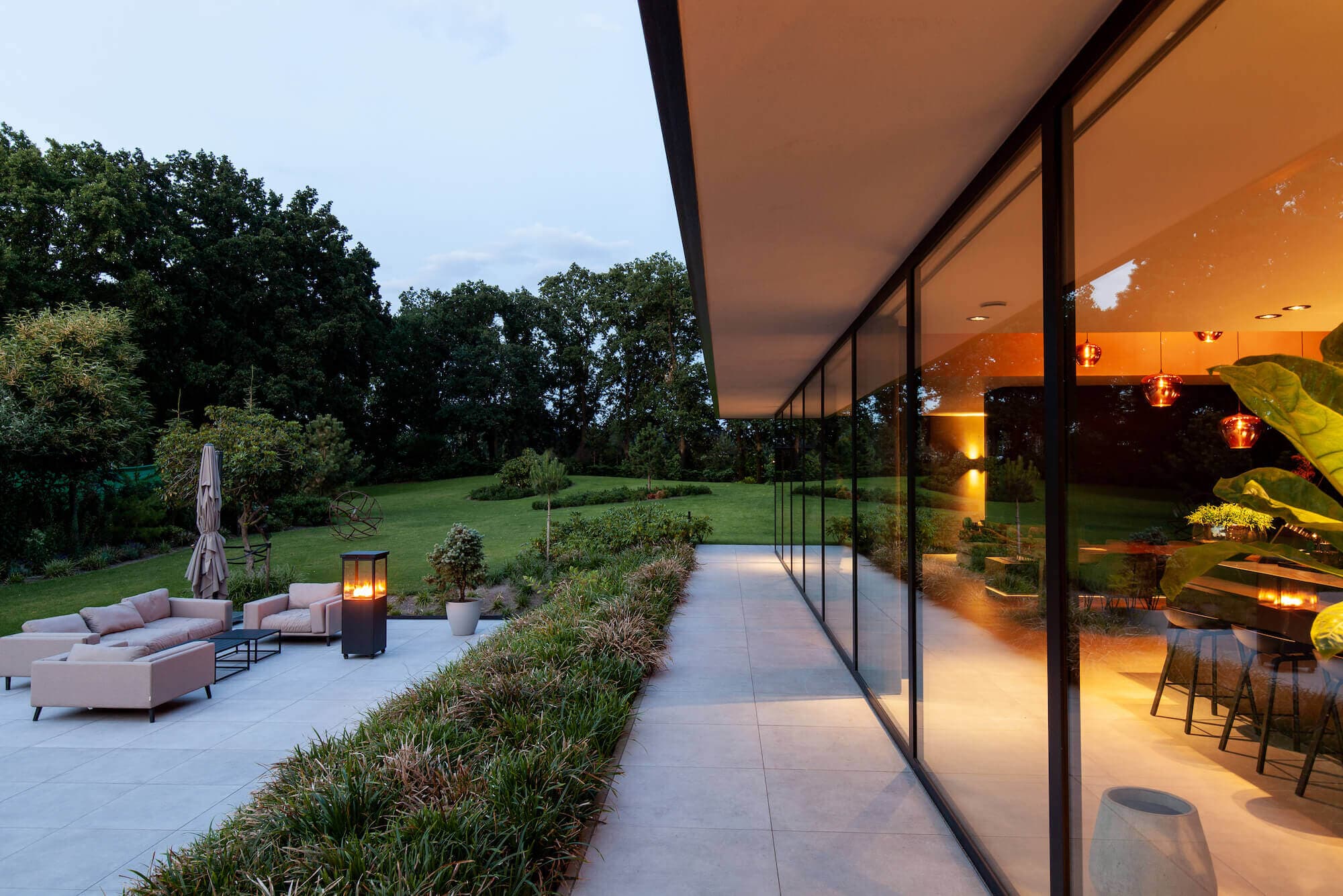 Tuinzijde villa met loungehoek, grasveld en verlichte gevel