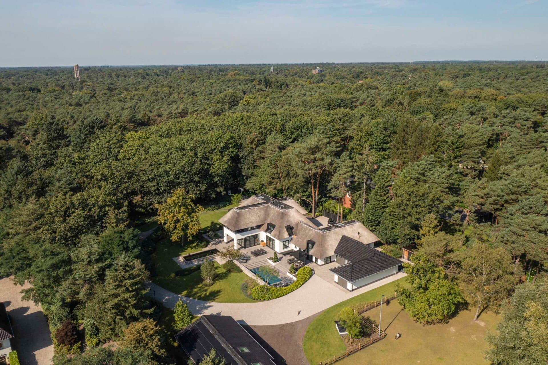 Luchtfoto villa met rieten dak, witte muren en aangelegde tuin