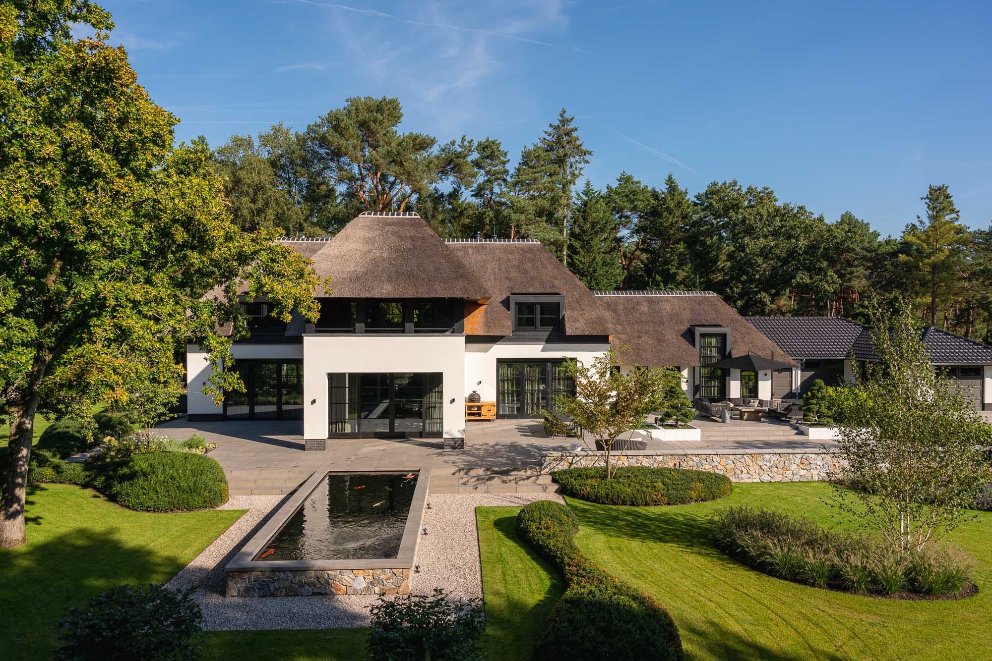 Zijgevel villa met rieten dak, witte muren en vijver in tuin