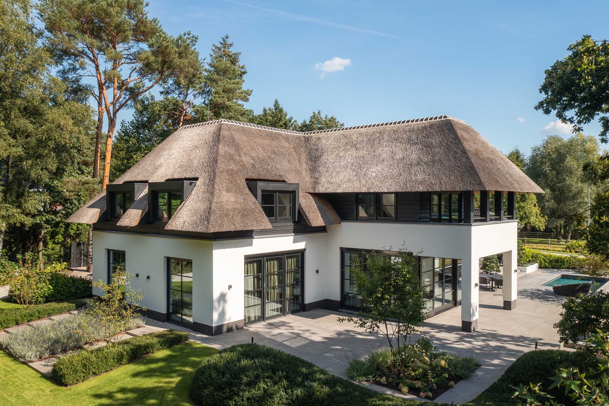 Voorgevel villa met rieten dak, witte muren en zwarte raamwerk