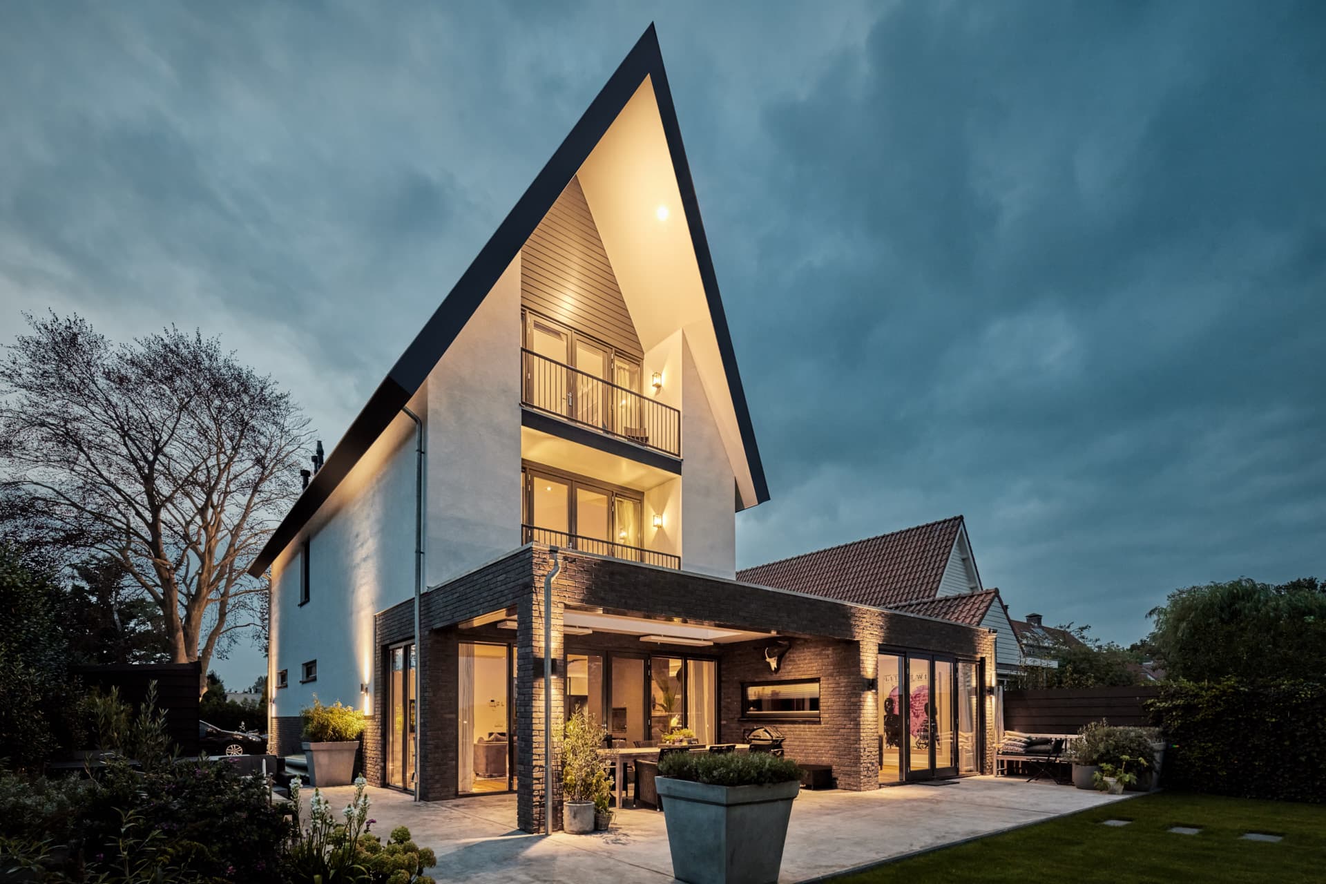 Verlichte villa met driehoekig dak en brede terras bij schemering