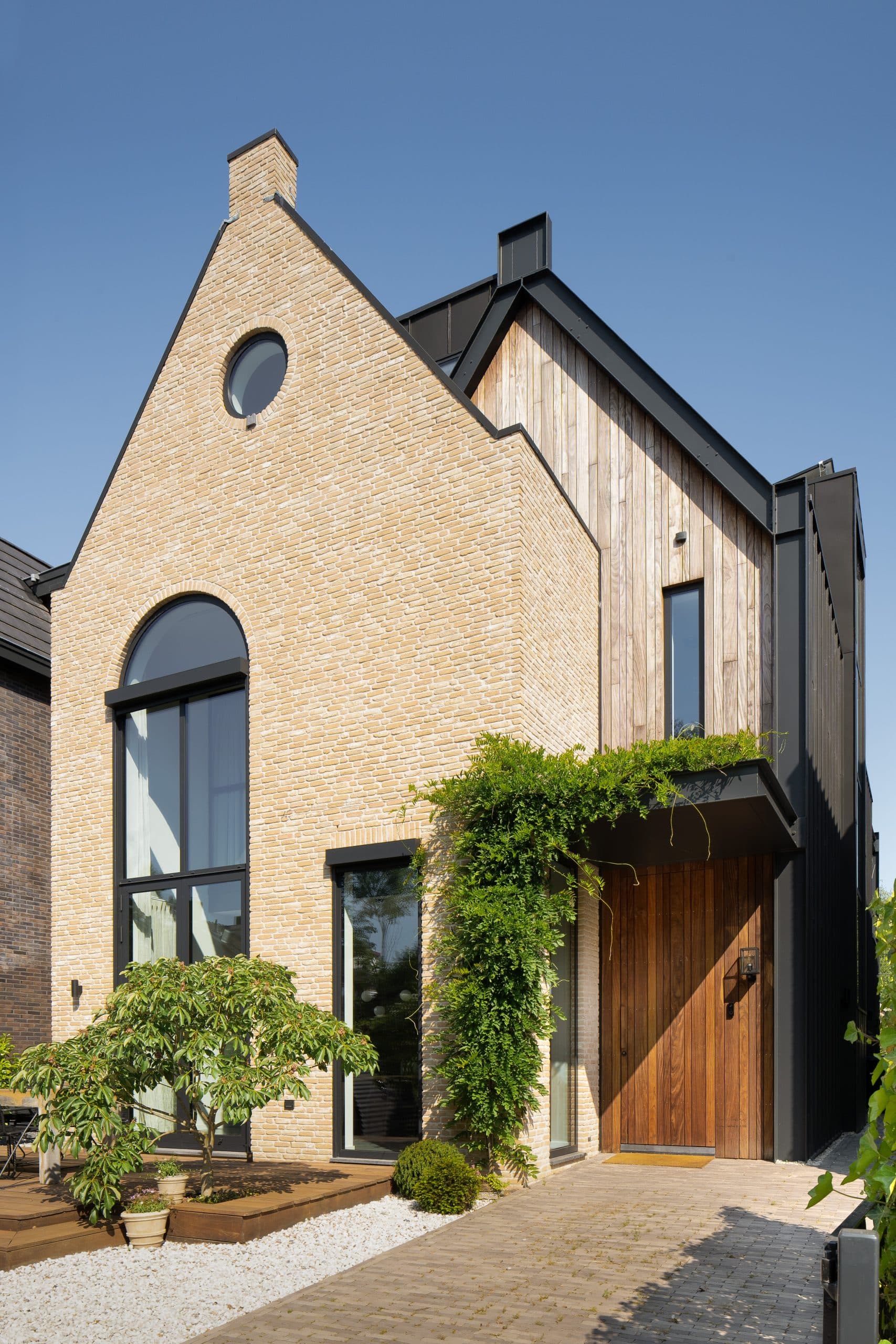 Voorgevel baksteenhuis met getrapt dak en houten voordeur, beplanting
