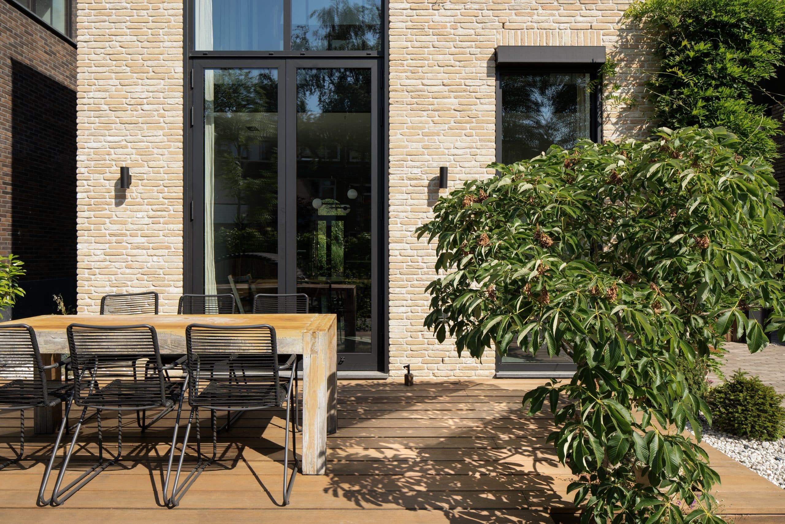Moderne entree met houten deur onder zwart afdak, baksteengevel
