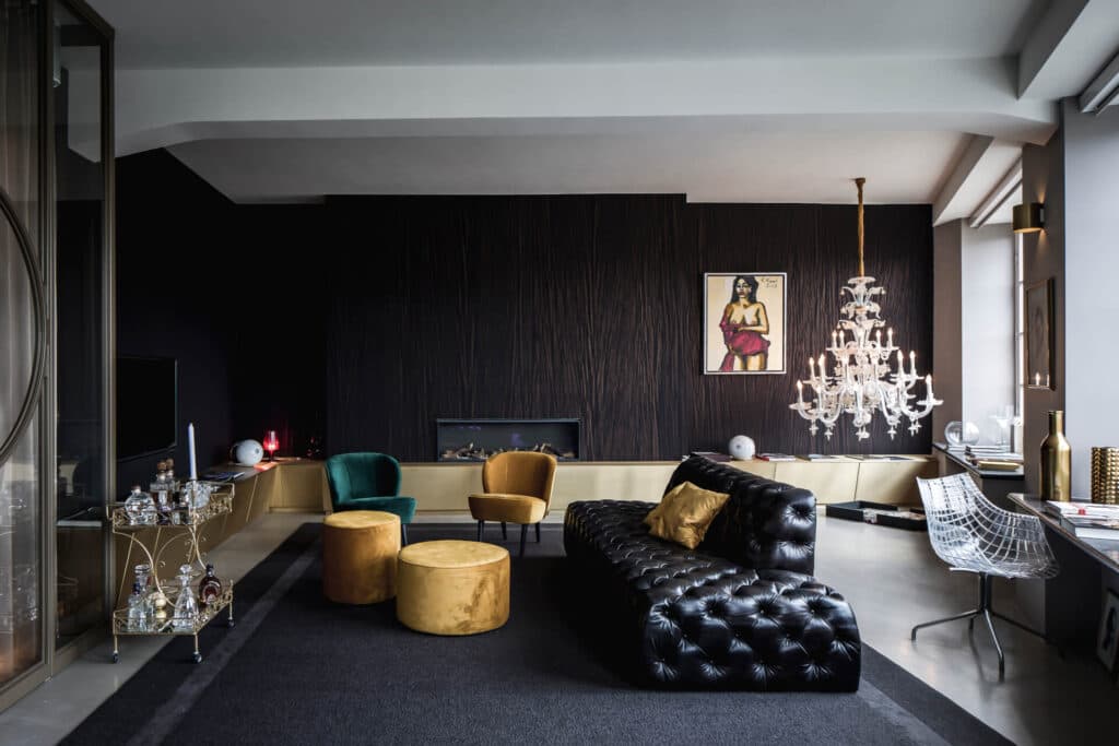 Woonkamer met zwarte leren bank, gele velours fauteuils en open haard