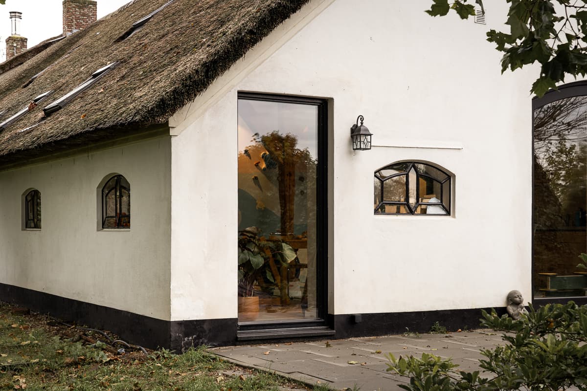 Witte cottage met rieten dak, grote zwarte ramen en terracotta tegels