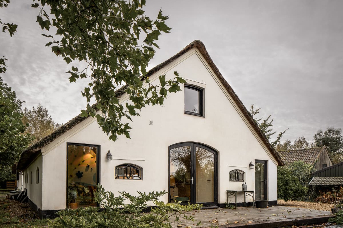 Witte woning met rieten dak, zwarte ramen en natuurstenen terras